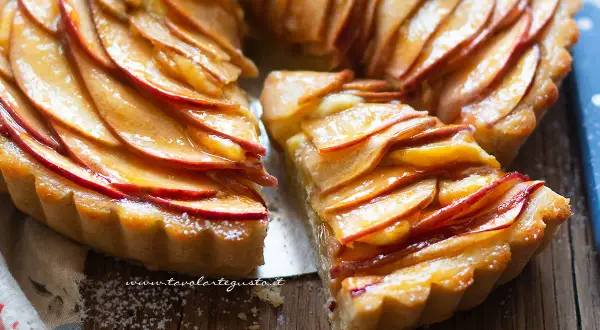 Una fetta di crostata di mele dorata, con mele caramellate disposte a spirale su una base friabile.