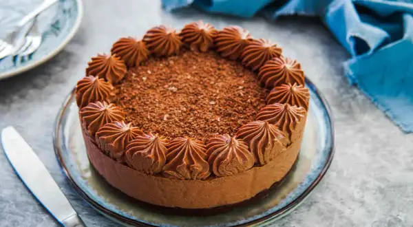 Delizioso cheesecake al cioccolato con decorazioni a ciuffi e scaglie di cioccolato. Un coltello da burro è pronto per essere usato.