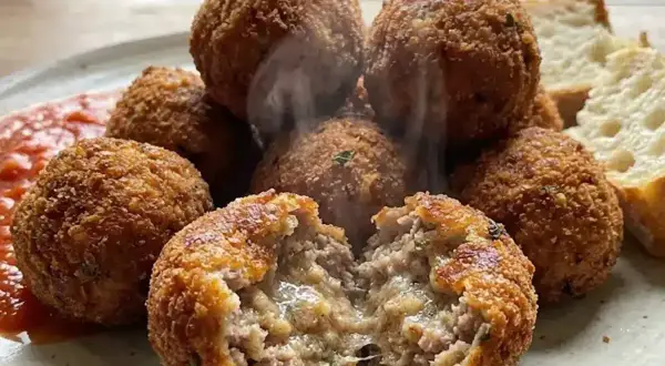 Polpette al forno dorate e croccanti, una aperta rivela un interno succulento. Servite con salsa rossa e pane.
