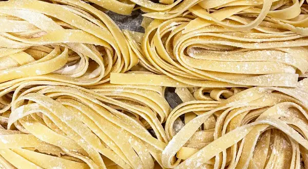 Un primo piano di **tagliatelle fatte in casa**, fresche e spolverate di farina, pronte per essere cucinate.
