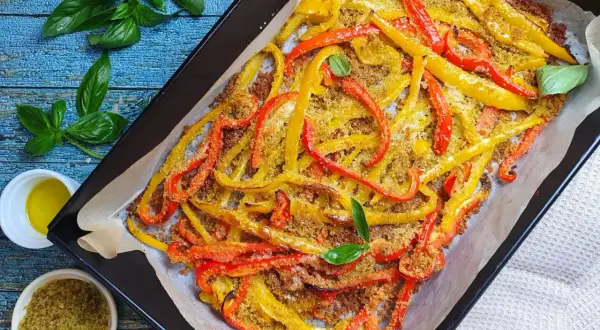 Peperoni al forno tagliati a listarelle, dorati e croccanti, conditi con pangrattato e basilico fresco.