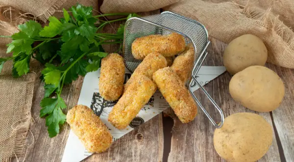 Crocchette di patate in friggitrice ad aria, dorate e croccanti, pronte per essere gustate. Accanto, patate fresche e prezzemolo.