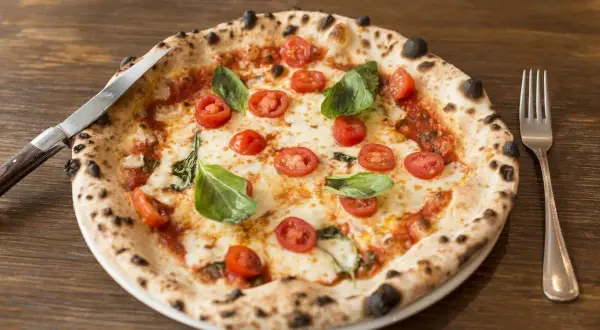 Pizza con lievito madre, pomodorini freschi, mozzarella filante e basilico profumato. Un capolavoro da gustare con coltello e forchetta.