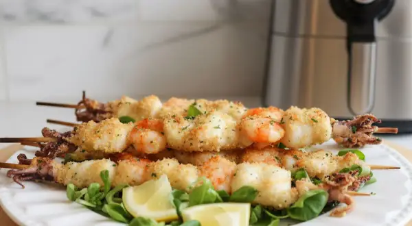 Spiedini di gamberi e calamari impanati, cotti alla perfezione nella friggitrice ad aria. Serviti su un letto di insalata con spicchi di limone.