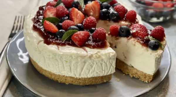 Deliziosa torta fredda allo yogurt, guarnita con fragole, lamponi, mirtilli e una cascata di marmellata. Perfetta per un dessert estivo.
