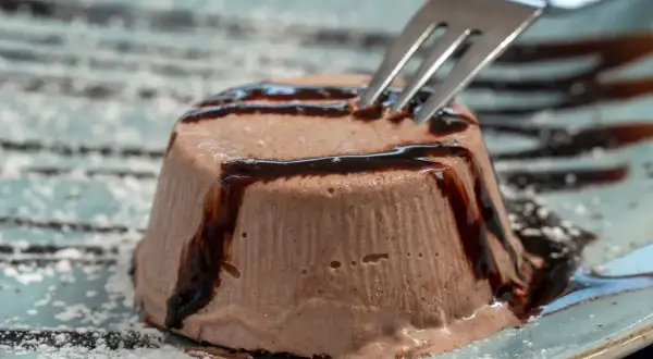 Un delizioso semifreddo al cioccolato, guarnito con sciroppo al cioccolato e spolverato di zucchero a velo, pronto per essere gustato con una forchetta.