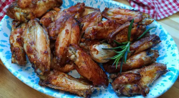 Alette di pollo al forno dorate e succulente, servite su un piatto decorato con un rametto di rosmarino.