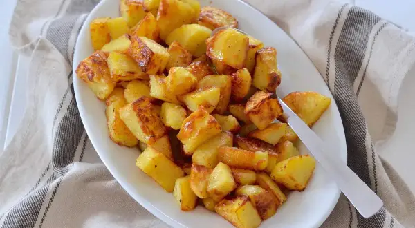 Un piatto bianco pieno di patate al forno dorate e croccanti, pronte per essere gustate.