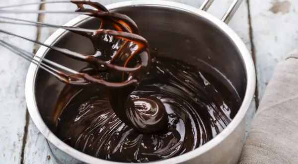 Una frusta mescola una lucida crema al cioccolato in una pentola d'acciaio.