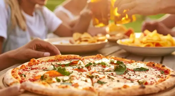 Una deliziosa pizza fatta in casa, tagliata a fette, pronta per essere gustata con amici e birra fresca all'aperto.