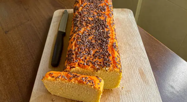 Pane di lenticchie con semi di lino in cima, su tagliere di legno. Una fetta è già stata tagliata.