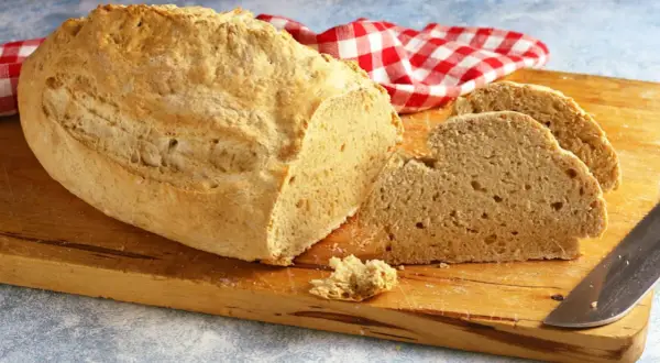 Pane casereccio con lievito istantaneo, tagliato su un tagliere di legno, con un tovagliolo a quadri rossi e bianchi.