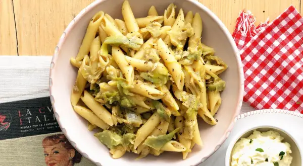 Penne con carciofi, un piatto che Antonino Cannavacciuolo saprebbe preparare alla perfezione, servito in una ciotola rosa.