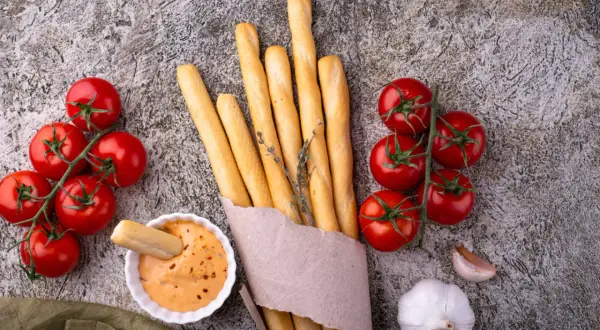 Grissini fatti in casa dorati, con pomodorini freschi, aglio e una salsa cremosa. Perfetti per un aperitivo rustico.
