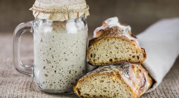 Un barattolo di lievito madre attivo e fette di pane rustico, pronti per creare deliziosi impasti. Ecco come si fa il lievito madre.