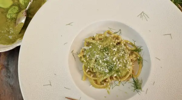 Un piatto di pasta condita con un cremoso macco di fave fresche, guarnito con aneto e formaggio grattugiato.