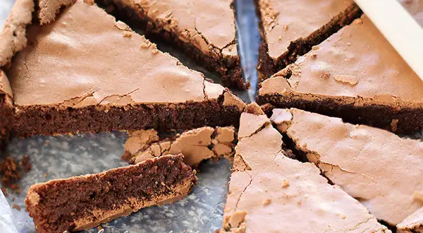 Una deliziosa torta al cioccolato fondente, tagliata a fette triangolari, con una crosta leggermente screpolata e un interno umido e invitante.