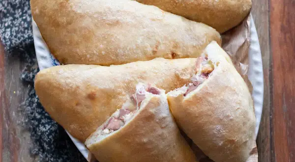 Calzoni al forno dorati e fragranti, ripieni di prosciutto e formaggio filante, pronti per essere gustati.