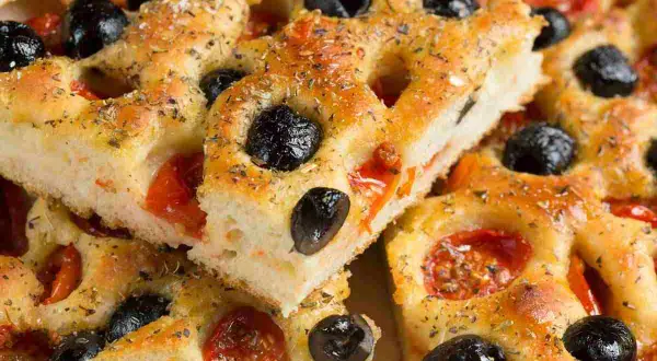 Focaccia pugliese ricetta originale sofficissima, con pomodorini e olive nere, condita con erbe aromatiche.
