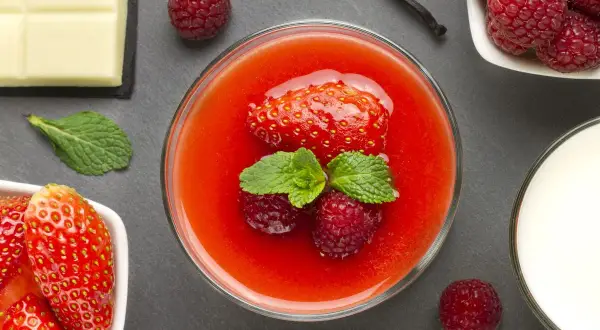 Un bicchiere di coulis di fragole con fragola, lamponi e menta. Accanto, cioccolato bianco, lamponi freschi e un bicchiere di latte.