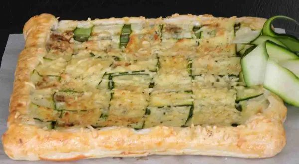 Torta salata con pasta sfoglia e zucchine, gratinata al forno e guarnita con fettine di zucchina fresca.