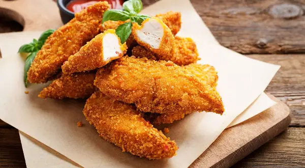 Bocconcini di pollo in friggitrice ad aria, dorati e croccanti, serviti con basilico fresco e salsa.