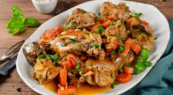 Un saporito coniglio in umido con carote e erbe aromatiche, servito su un piatto bianco.