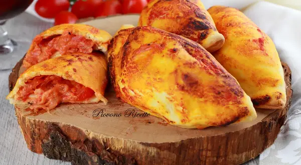 Panzerotti al forno dorati e ripieni di pomodoro e formaggio filante, serviti su un tagliere di legno.