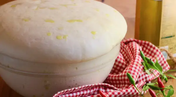 Impasto lievitato per pizza con lievito di birra, pronto per essere infornato. Olio d'oliva e peperoncini completano la scena.
