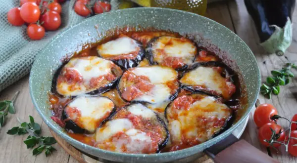 Fette di melanzane cotte in padella con pomodoro e mozzarella filante, un classico piatto di melanzane alla pizzaiola.
