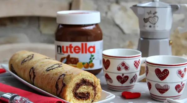 Rotolo alla Nutella pronto per essere gustato, con una moka e due tazze a tema cuore.