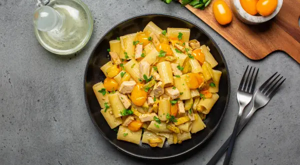 Piatto di pasta con pesce spada, pomodorini gialli e zucchine, guarnito con prezzemolo fresco.