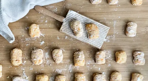 Gnocchi di zucca fatti in casa, pronti per essere cotti, sparsi su un tagliere di legno con un rigagnocchi.