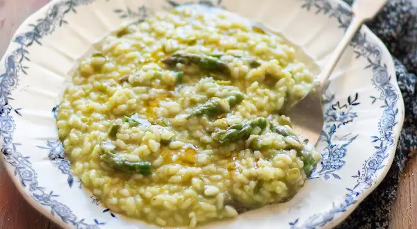 Un cremoso risotto con asparagi, servito su un piatto decorato. Un piatto primaverile che profuma di buono.