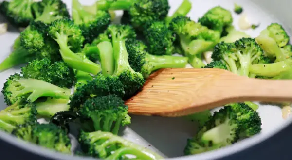 Broccoli in padella, con un mestolo di legno che mescola le cimette verdi e brillanti, pronte per essere gustate.