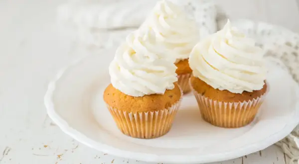 Tre cupcake su un piatto bianco, decorati con abbondante crema al burro soffice e ariosa.