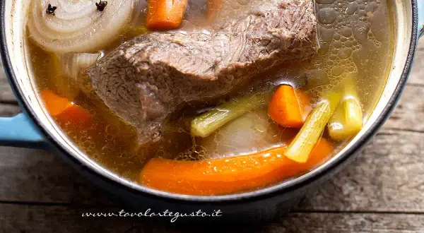 Un pezzo di carne succulenta cuoce lentamente in un brodo di carne aromatico, con carote, sedano e cipolla.
