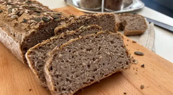 Fetta di pane di grano saraceno, cosparso di semi, su tagliere di legno.