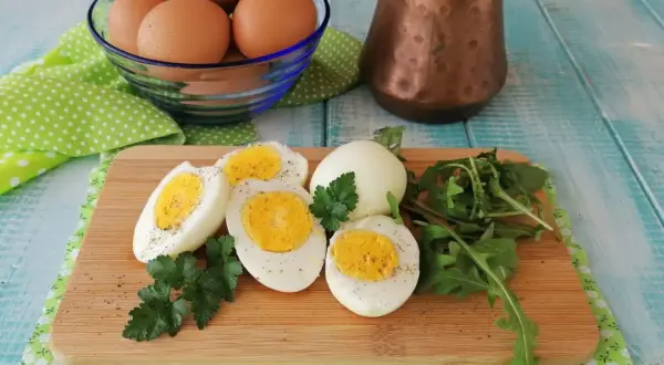 Uova sode in friggitrice ad aria, tagliate a metà, con un ciuffo di prezzemolo e rucola su un tagliere di legno.