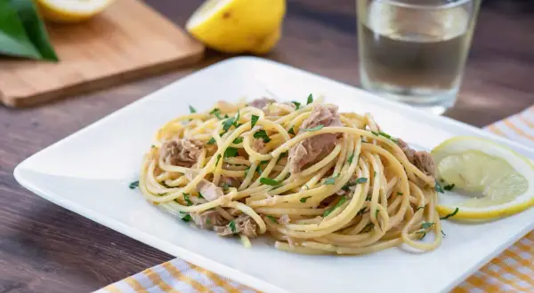 Un piatto di pasta tonno e limone, guarnito con prezzemolo fresco e spicchi di limone, pronto per essere gustato.