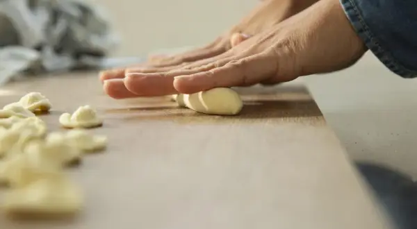 Mani che modellano impasto per creare orecchiette fatte in casa su un tagliere di legno.