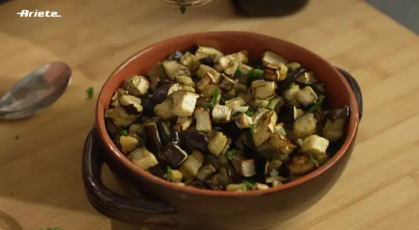 Melanzane in friggitrice ad aria, tagliate a cubetti e condite con erbe aromatiche, servite in una ciotola di terracotta.