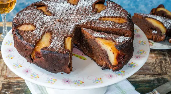 Torta al cioccolato e pere, cotta in friggitrice ad aria, spolverata di zucchero a velo. Una fetta è già servita.