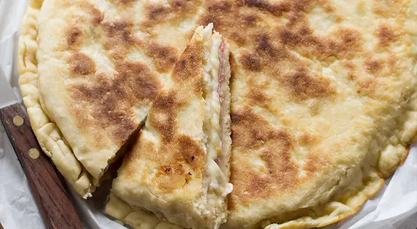 Focaccia in padella dorata e fragrante, farcita con formaggio e salumi, tagliata a spicchi.
