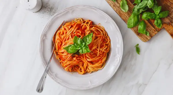 Un piatto di spaghetti al sugo di pomodorini freschi, guarnito con basilico, pronto per essere gustato.