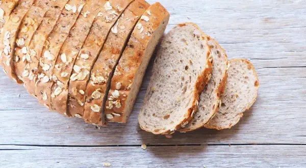 Pane fatto in casa ricetta della nonna, con crosta dorata e semi, affettato su un tavolo di legno.