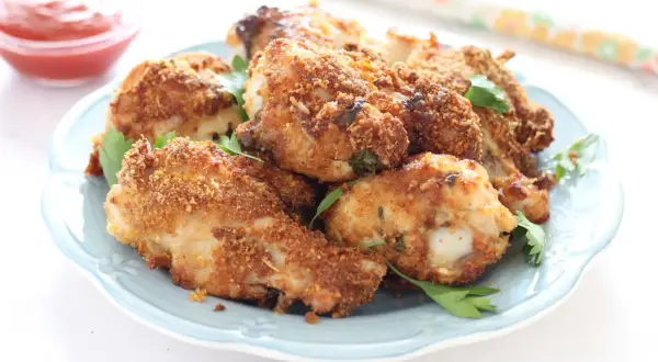 Alette di pollo croccanti in friggitrice ad aria, servite su un piatto azzurro con prezzemolo fresco e una ciotolina di ketchup.