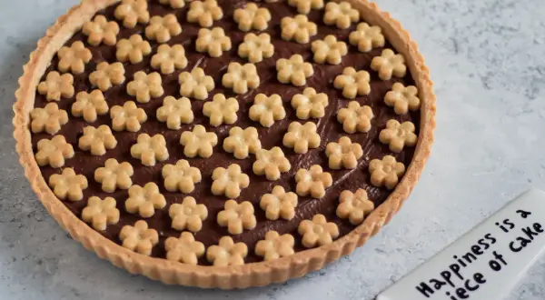Deliziosa crostata alla nutella con decorazioni a forma di fiorellini. Un dolce che porta gioia, come dice la spatola: "Happiness is a piece of cake".