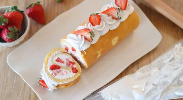 Rotolo panna e fragole decorato con panna montata e fragole fresche, pronto per essere gustato.
