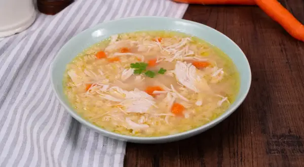 Un confortevole brodo di pollo con pezzi di pollo sfilacciato, carote e un rametto di prezzemolo.